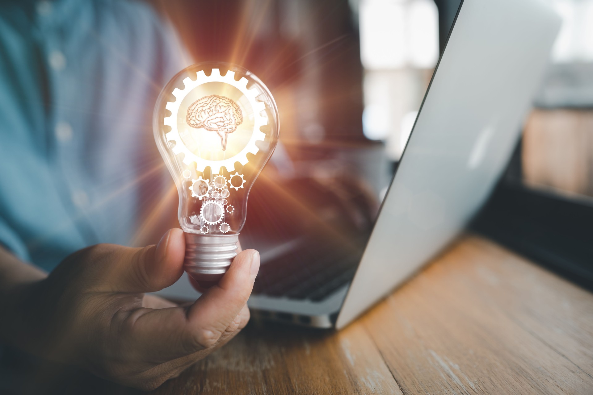 The hand of a man with a light bulb And there is a gear icon and brain in it And he is using a notebook computer. The idea of ​​inspiration from online technology.innovation idea concept.